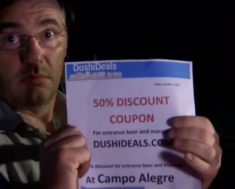 Figurant toont de kortingsbon van DushiDeals.com uit de campagne van 2016: 50% discount coupon voor entree, bier en massage bij Campo Alegre